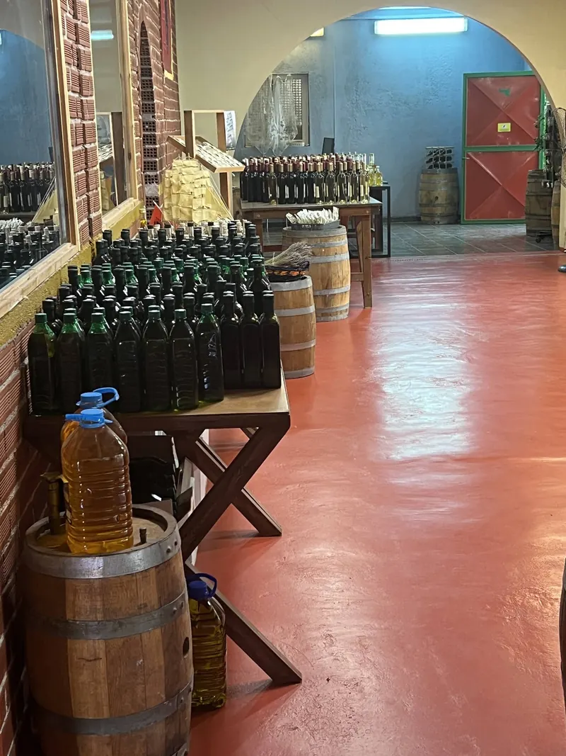 Bottles of wine and olive oil lined up beside oak barrels